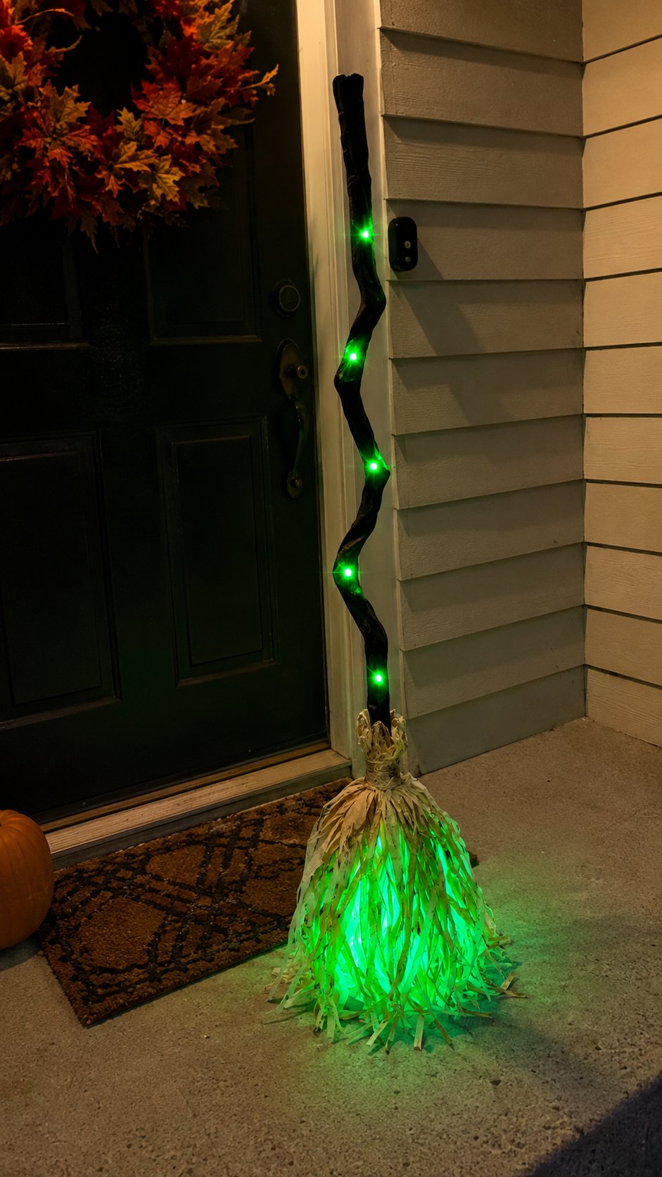 Customer-style photo of the illuminated Halloween broom beside a front door